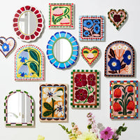 Collection of colorful decorative tiles and mirrors on a white wall with floral arrangements.